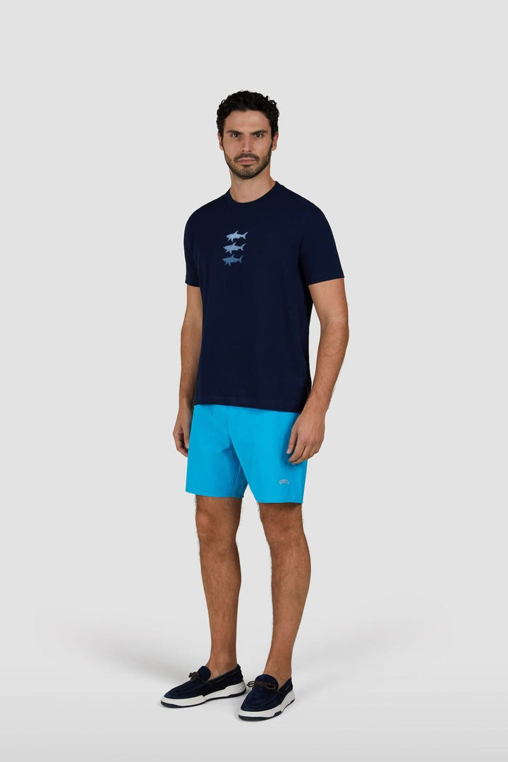 T-shirt en coton marine avec imprimé requins, porté par un homme en shorts bleus et chaussures noires.
