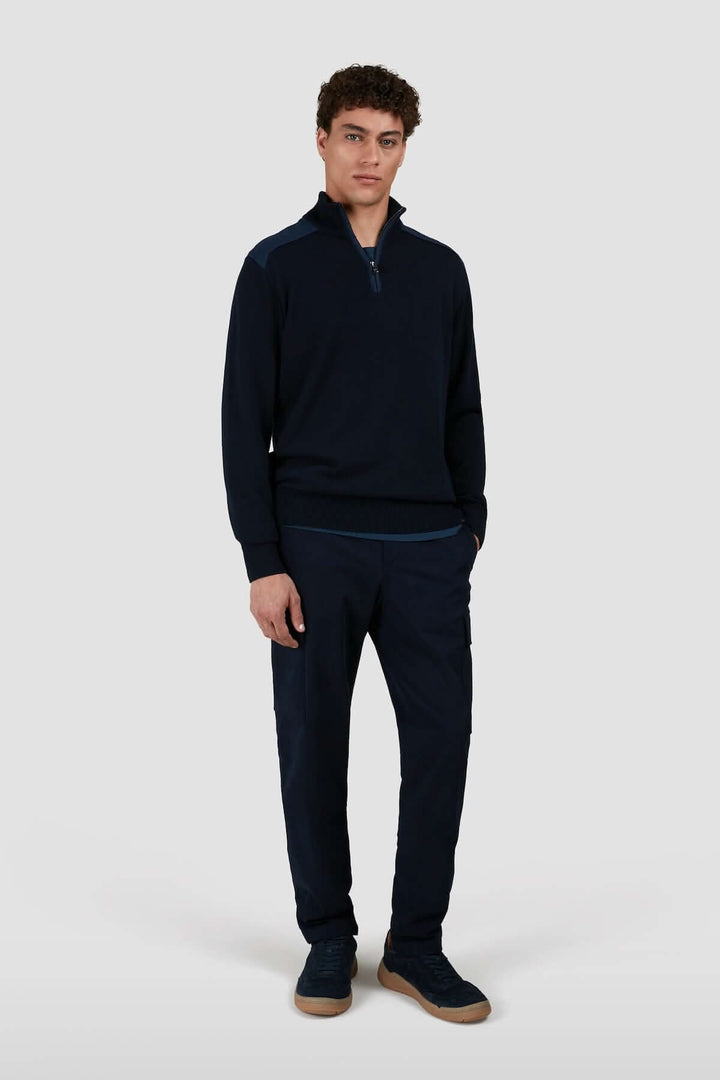 Homme en tenue décontractée, portant un pull bleu marine à col zippé et pantalon assorti.