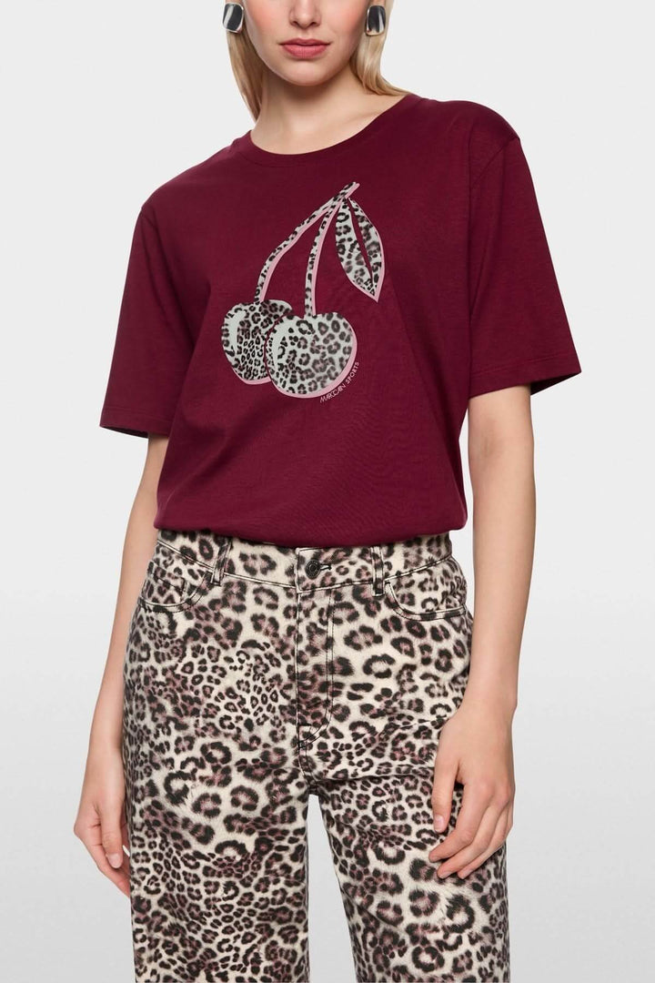 Femme portant un T-shirt imprimé cerises léopard, style décontracté, en coton bio, moderne et tendance, label Rethink Together.