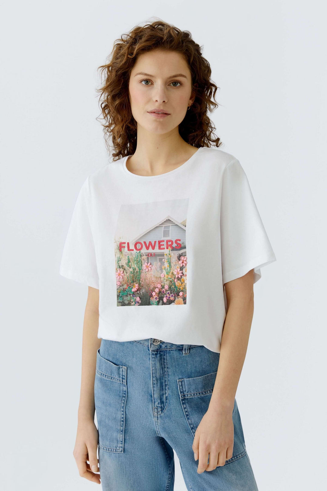 Femme portant un T-shirt imprimé graphique "Flowers", coupe droite et manches courtes, idéal pour un style décontracté et moderne.