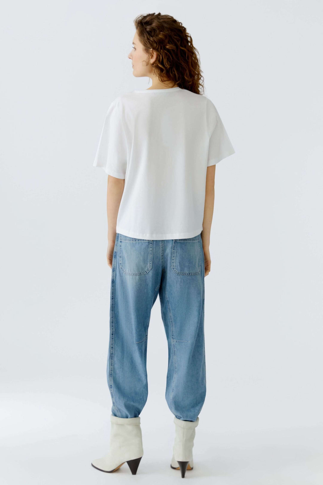 Personne portant un t-shirt imprimé graphique et un jean, vue de dos, avec des manches courtes et coupe décontractée.