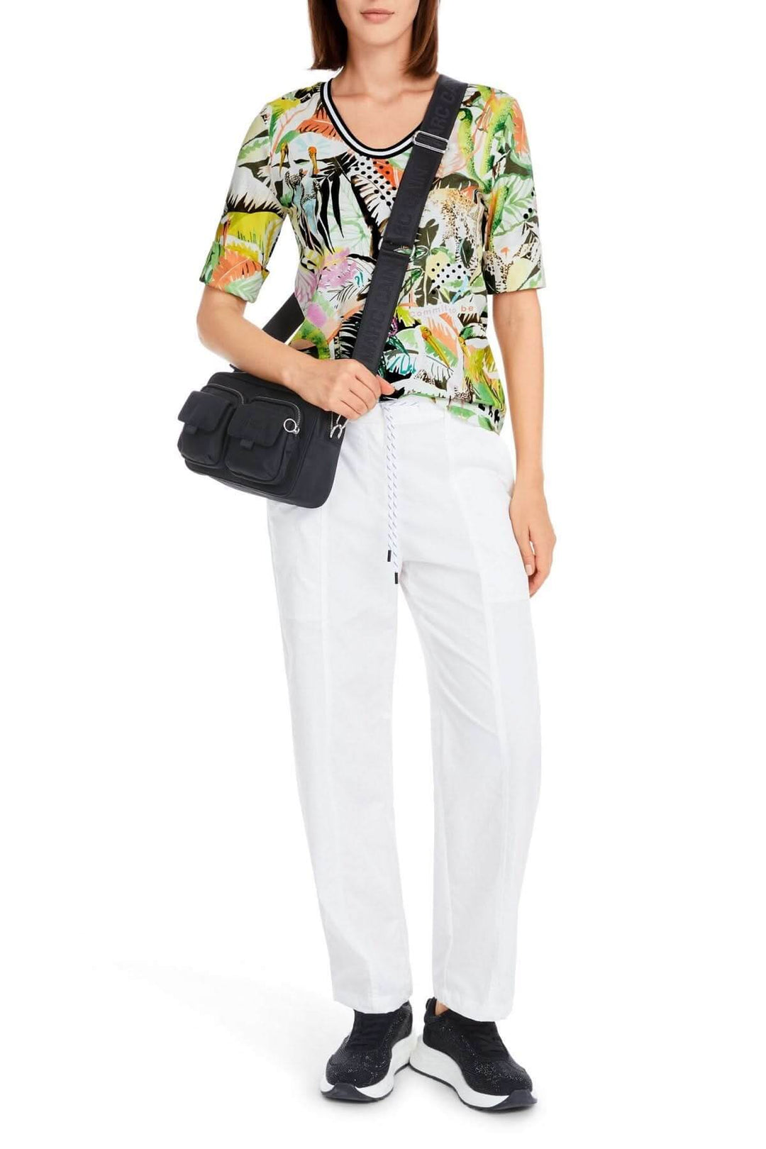 T-shirt imprimé jungle à manches 3/4, porté avec un pantalon blanc et un sac noir. Style décontracté et coloré.