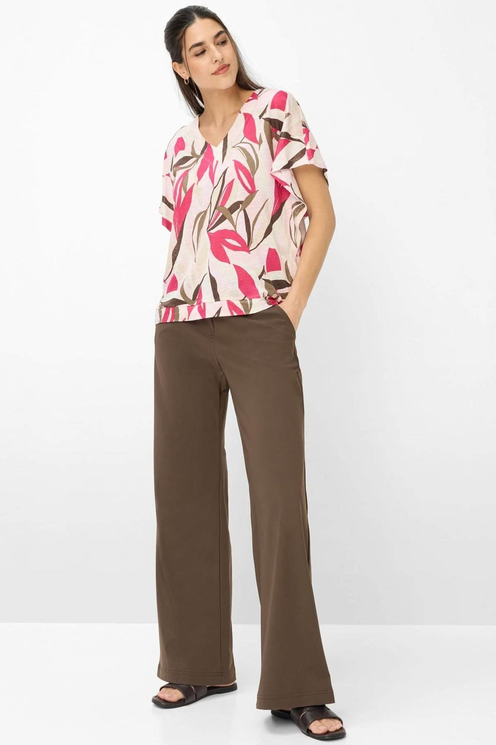 Femme portant le T-shirt imprimé végétal Cassie, coupe ample et encolure en V, avec un pantalon marron; style décontracté et moderne.
