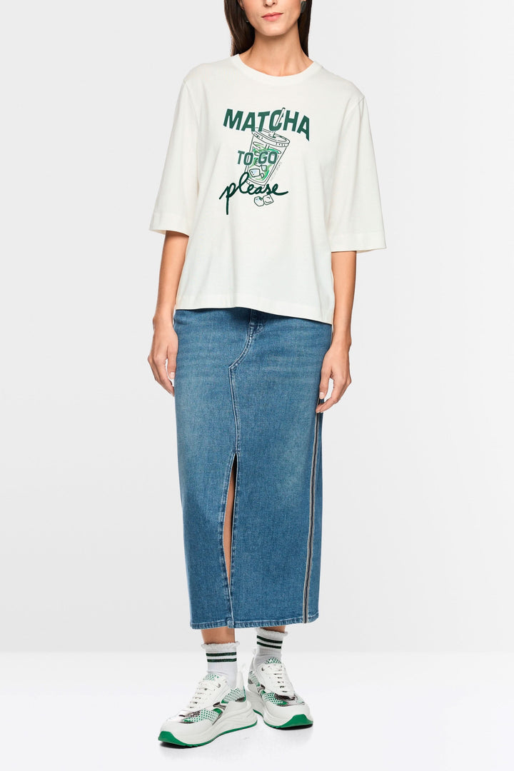 Femme portant un T-shirt imprimée matcha « Rethink Together » avec une jupe en jean et baskets blanches.