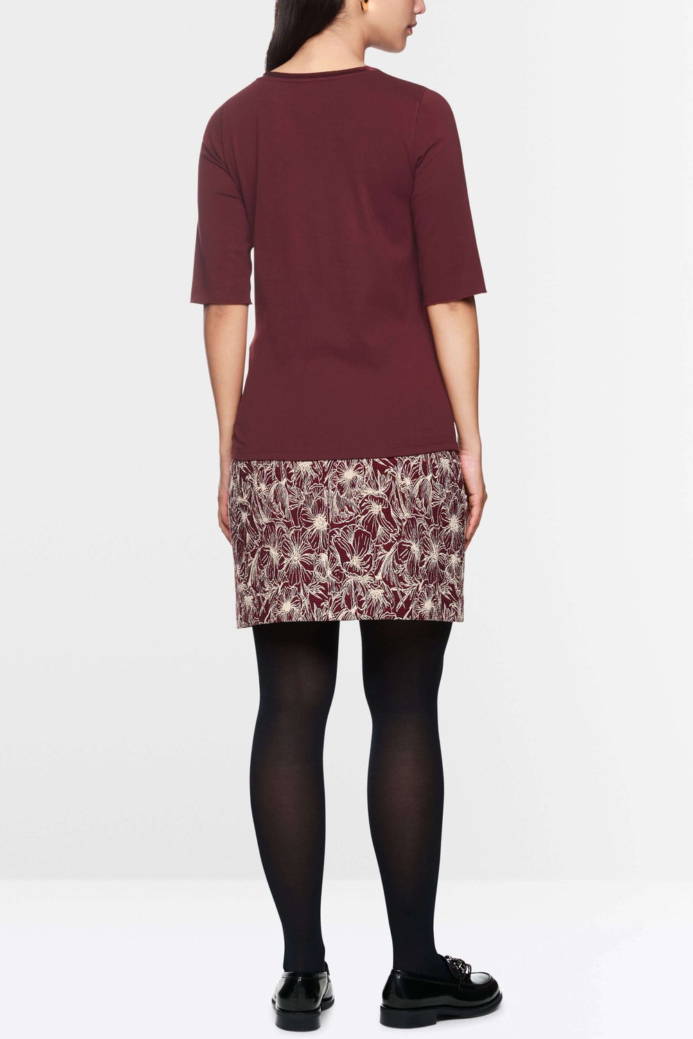 Vue arrière d'un T-shirt manches courtes bordeaux porté avec une jupe à motifs et des collants noirs.