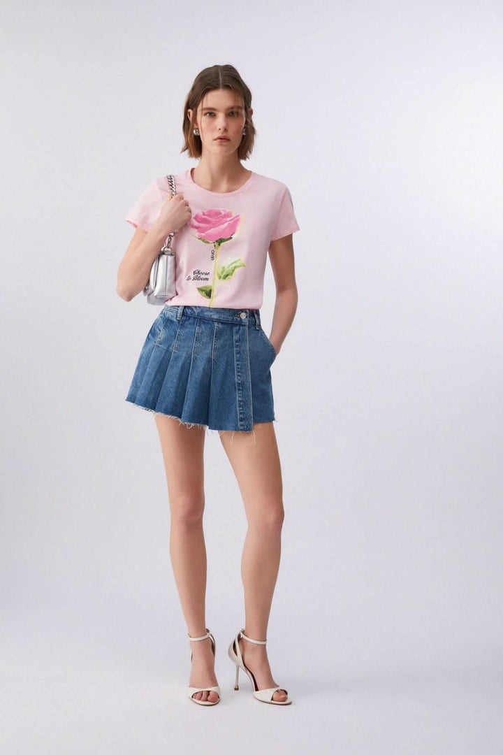 T-shirt à manches courtes avec imprimé graphique porté par une femme, complété par une jupe en jean et des sandales blanches.