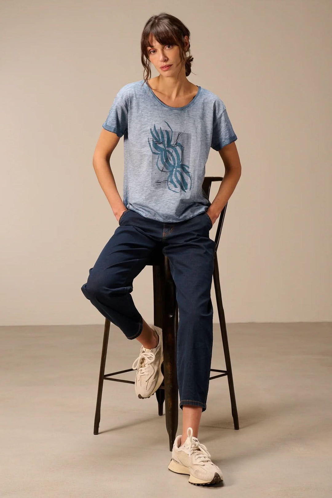 Femme portant un t-shirt à manches courtes coupe décontractée assise sur un tabouret, mettant en valeur un style décontracté moderne.