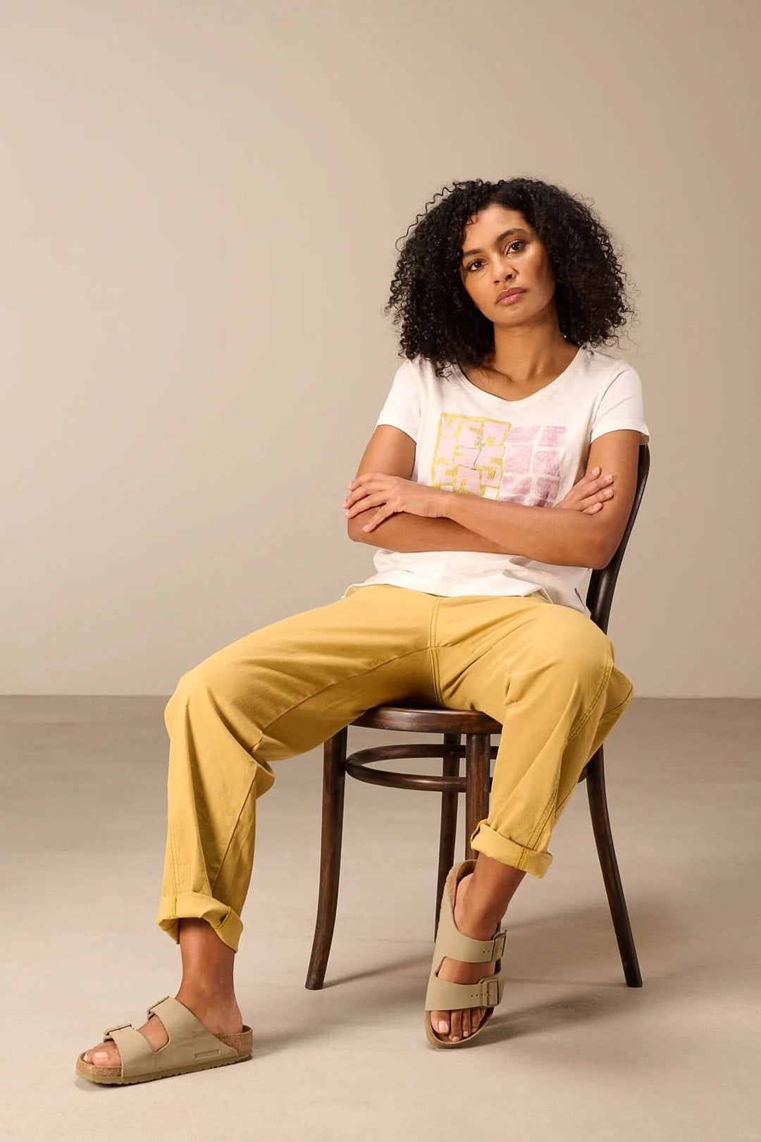 Femme portant un t-shirt à manches courtes coupe décontractée avec pantalon jaune, assise sur une chaise.