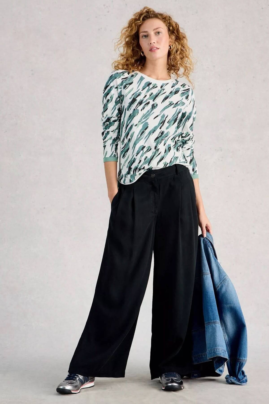 Femme portant un T-shirt à manches longues Clara avec pantalon ample noir, tenant une veste en jean.
