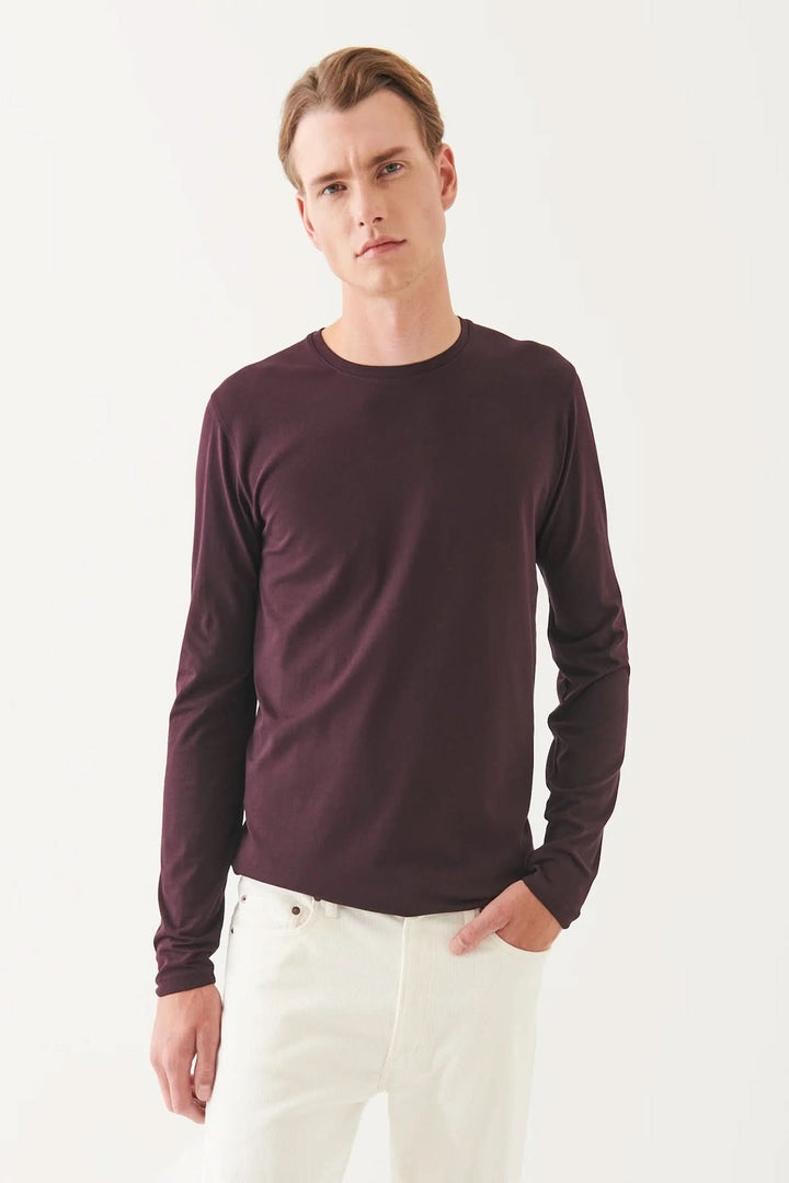 Homme portant un t-shirt manches longues en coton Pima péruvien, couleur bordeaux, avec pantalons blancs.