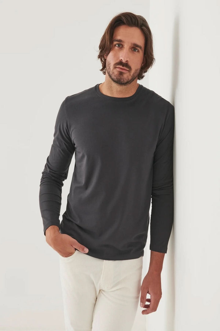 Homme portant un t-shirt à manches longues gris en coton Pima, contre un mur blanc.