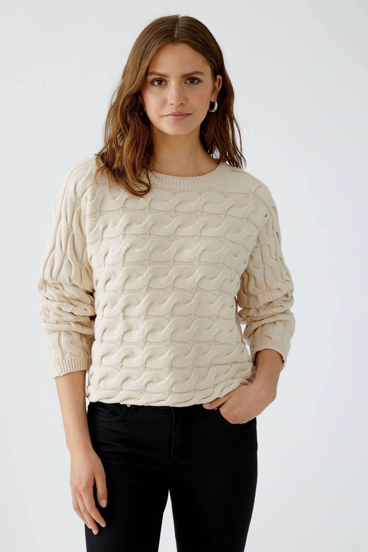Femme portant un Tricot Sirah avec motif torsadé et col bateau, confectionné en coton doux, allure moderne et élégante.