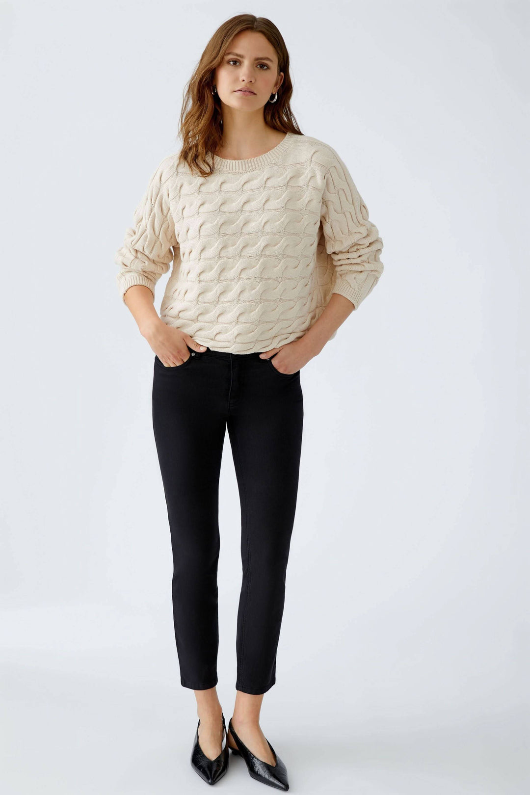 Modèle portant le Tricot Sirah à motif torsadé avec coupe carrée et col bateau élégant. Décris moi le produit en français.