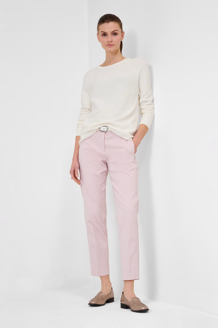 Femme en tricot blanc et pantalon rose, posant dans un cadre minimaliste, style automnal chic.