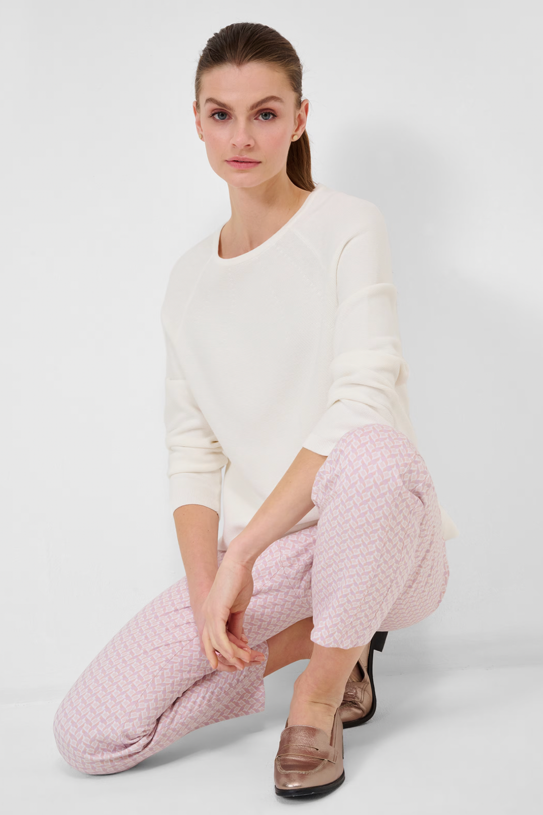 Femme assise portant un tricot blanc Lesley et pantalon à motifs roses, mode automnale élégante.