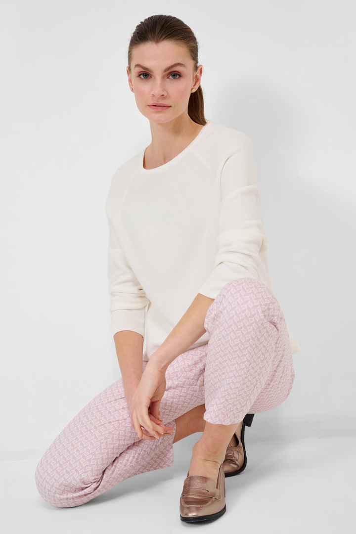 Femme assise portant un tricot blanc Lesley et pantalon à motifs roses, mode automnale élégante.