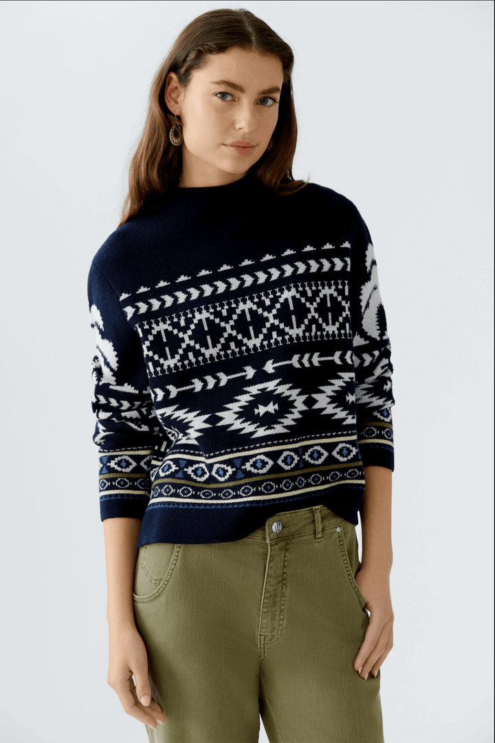 Tricot motif norvégien en jacquard avec col montant, manches longues et coupe décontractée, porté avec un pantalon vert.