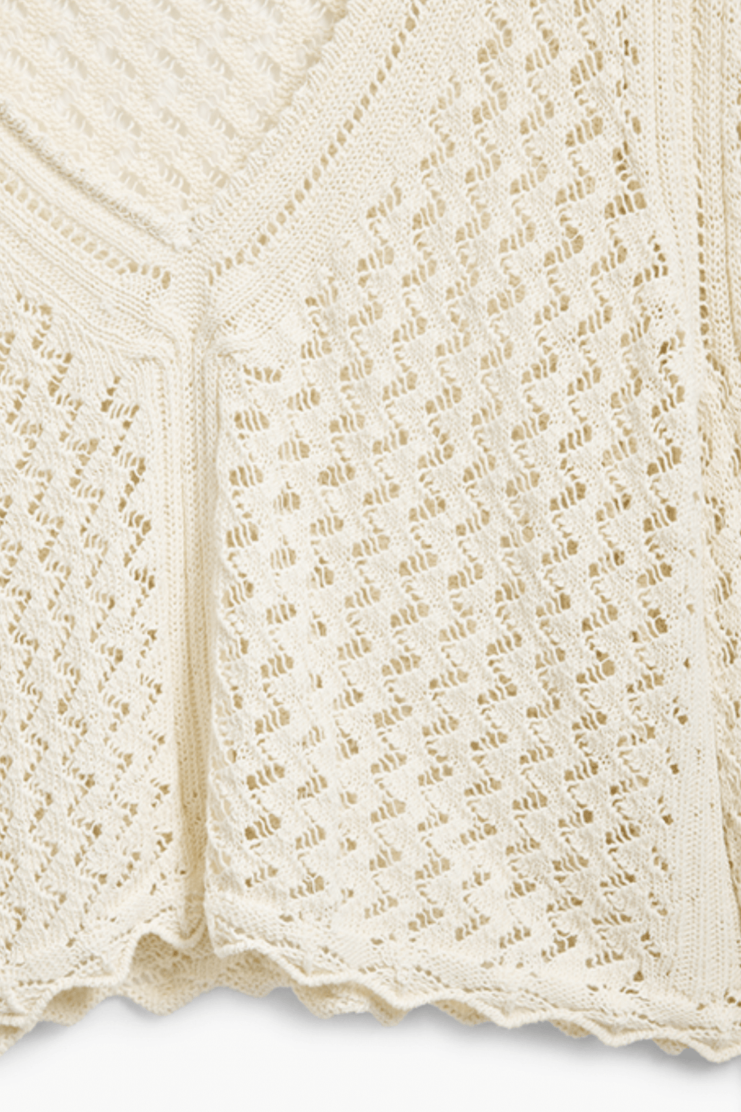 Tricot à motif ondulé en tissu ajouré, coloris crème, avec encolure en V et finitions délicates.