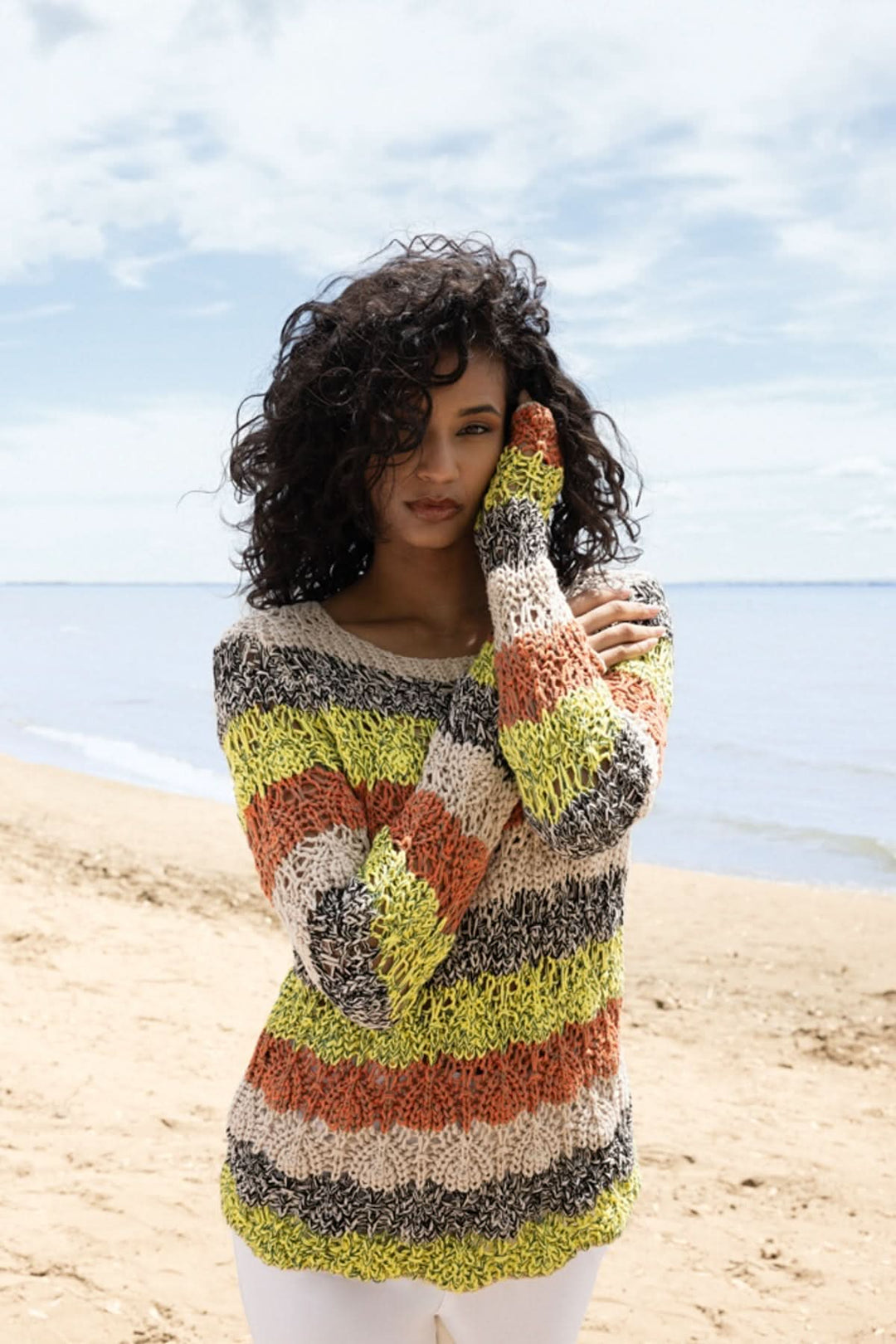 Femme portant un tricot rayé texturé coloré en bord de mer, parfait pour la mi-saison avec une coupe décontractée et finitions en coton.