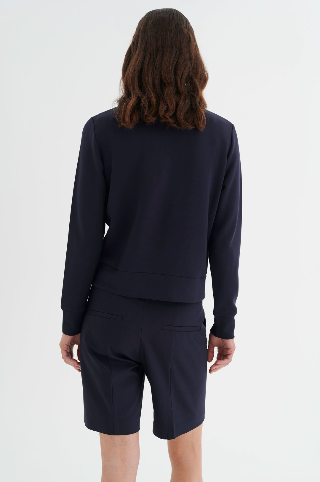 Vue arrière d'un modèle portant un ensemble de survêtement noir, composé d'un sweat et de shorts.