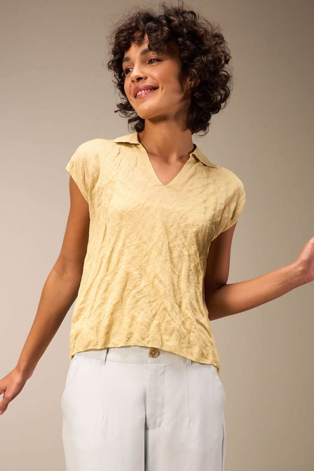 Veste décontractée à manches courtes et col en V, en tissu léger couleur jaune, portée avec un pantalon clair.