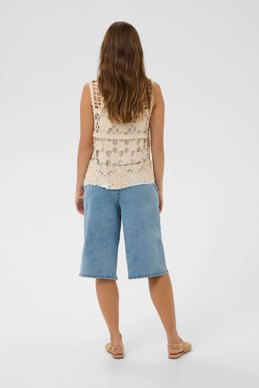 Modele portant une Veste Lotu sans manches en crochet, motif ajouré, vue arrière, tenue décontractée bohème chic pour l'été.