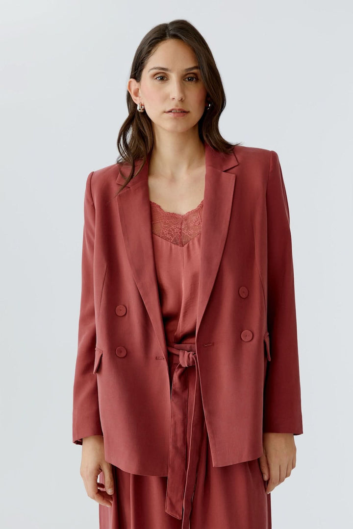 Femme portant une veste blazer structurée croisée rouge avec double boutonnage et coupe droite, idéale pour un look élégant et moderne.