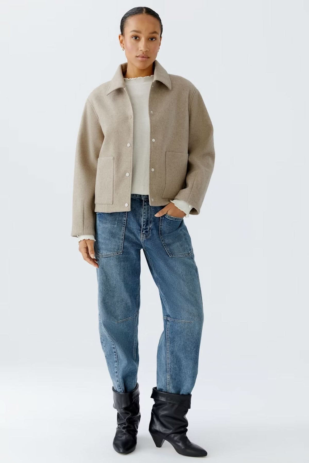 Femme portant une veste à coupe droite avec col classique, sur un chandail blanc, complété par un jean et des bottines noires, style casual chic.