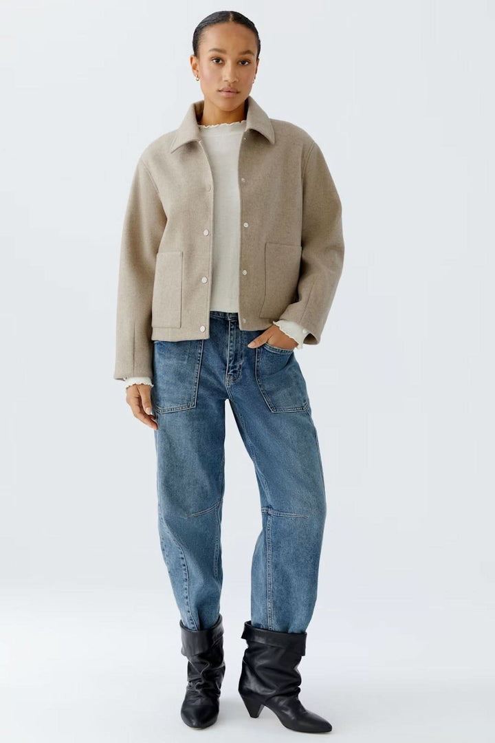 Femme portant une veste à coupe droite avec col classique, sur un chandail blanc, complété par un jean et des bottines noires, style casual chic.