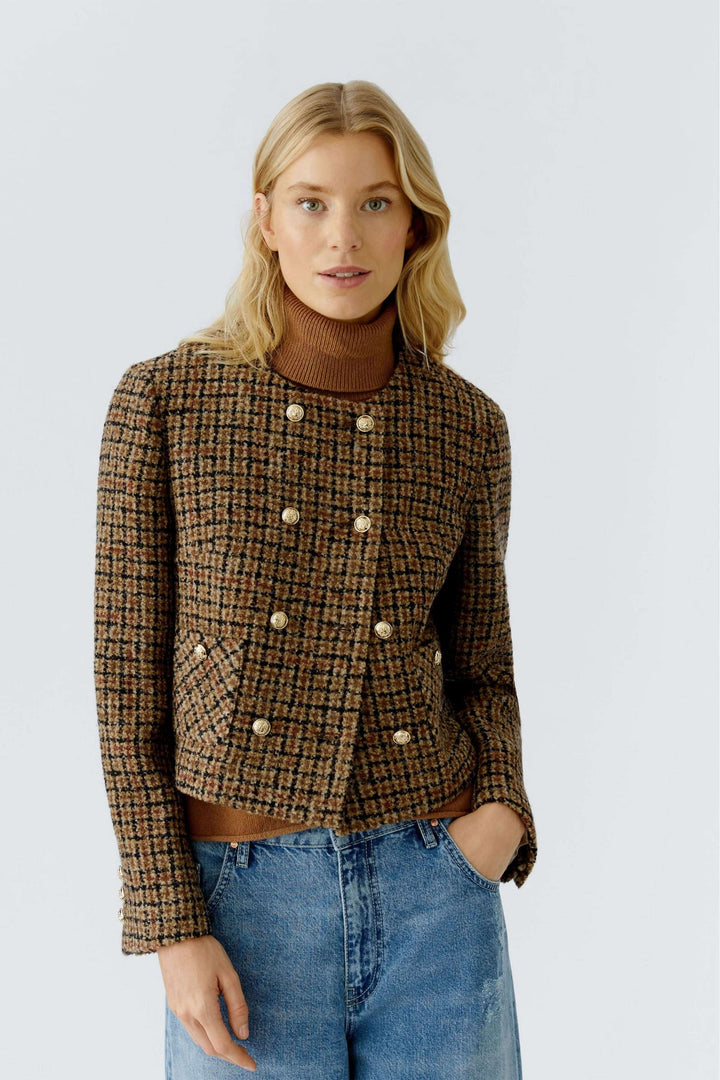 Femme portant une veste courte à carreaux, boutons dorés, avec motif texturé, associée à un jean et un col roulé brun.