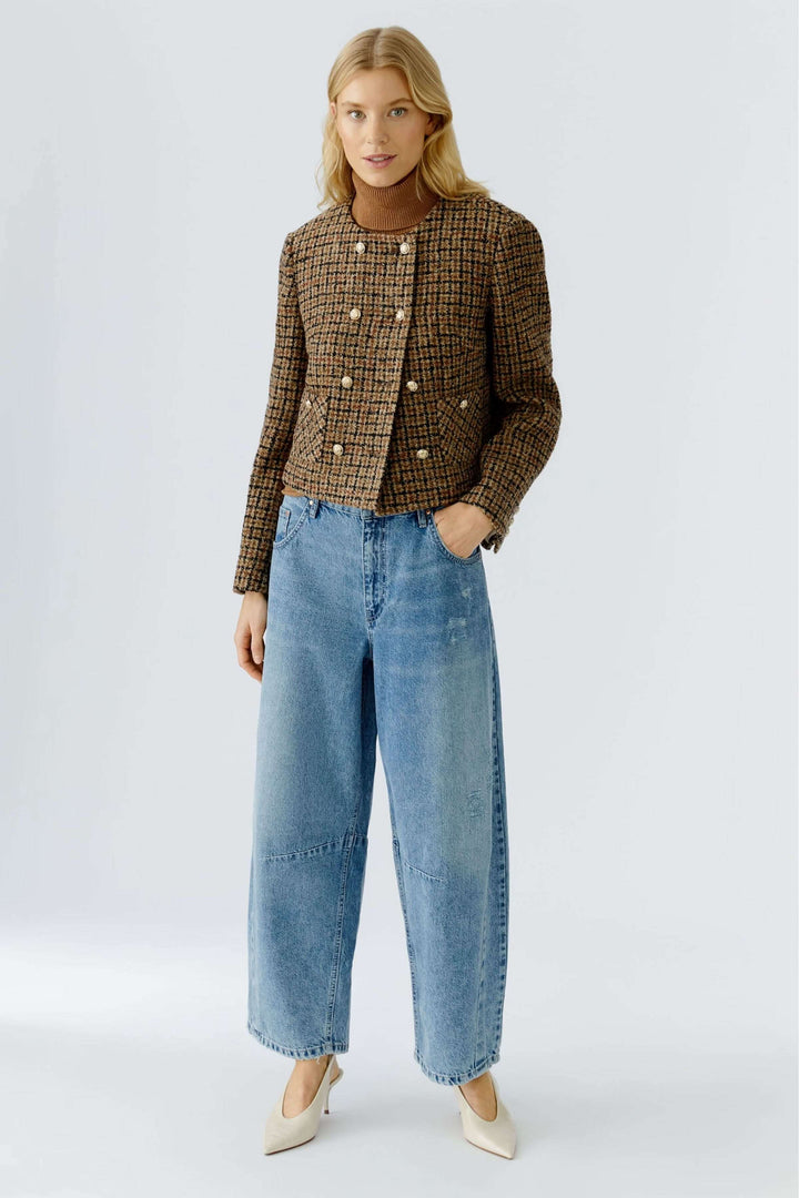 Femme portant une veste courte à carreaux, boutons dorés, en lainage texturé, avec un jean pour un look moderne et élégant.