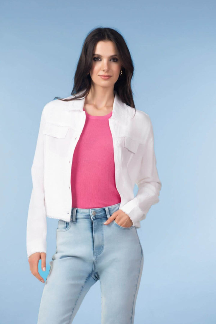 Femme portant une veste courte à finitions effilochées, avec un haut rose et un jean, sur fond bleu clair.
