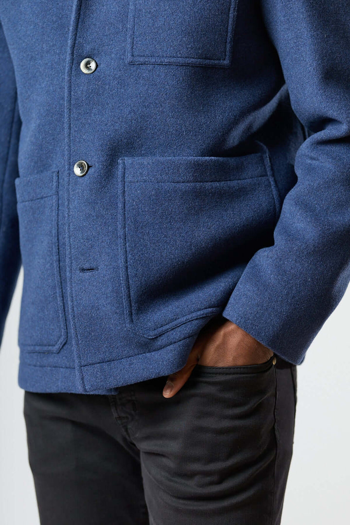 Homme portant une veste en laine à poches plaquées, couleur bleue, coupe droite et poches plaquées, style workwear élégant.
