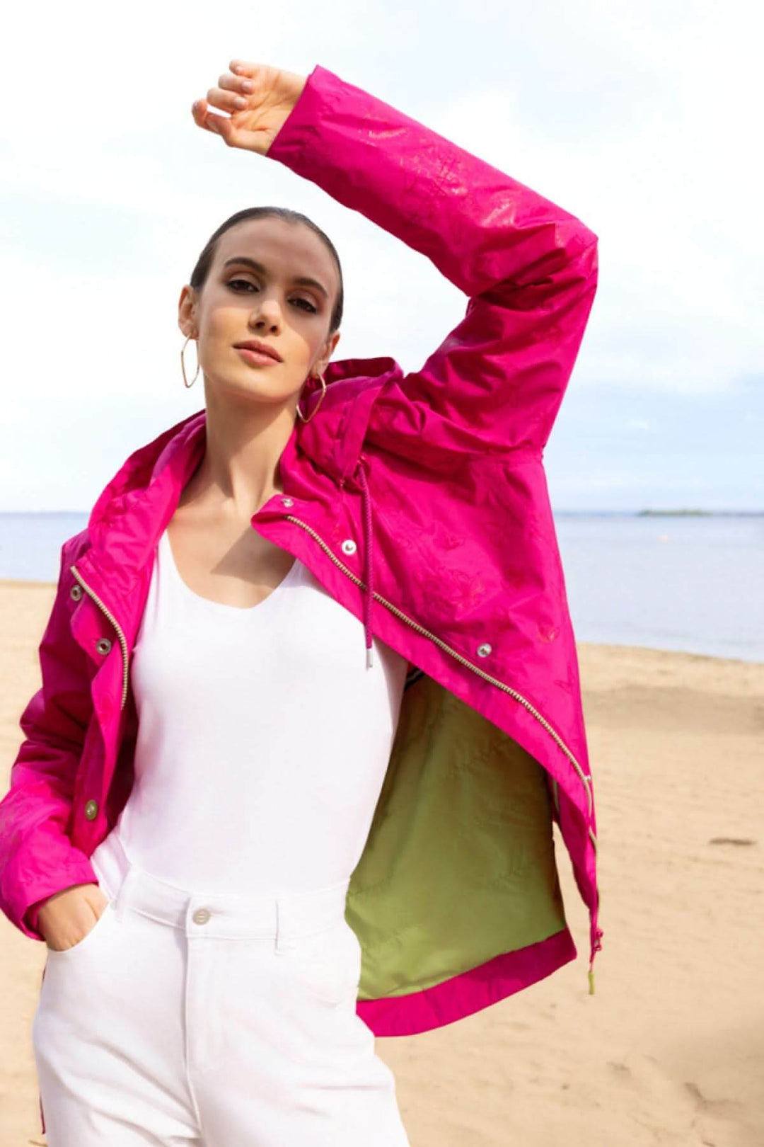 Veste légère à capuche rose portée sur la plage, offrant une silhouette moderne et protection contre les intempéries.
