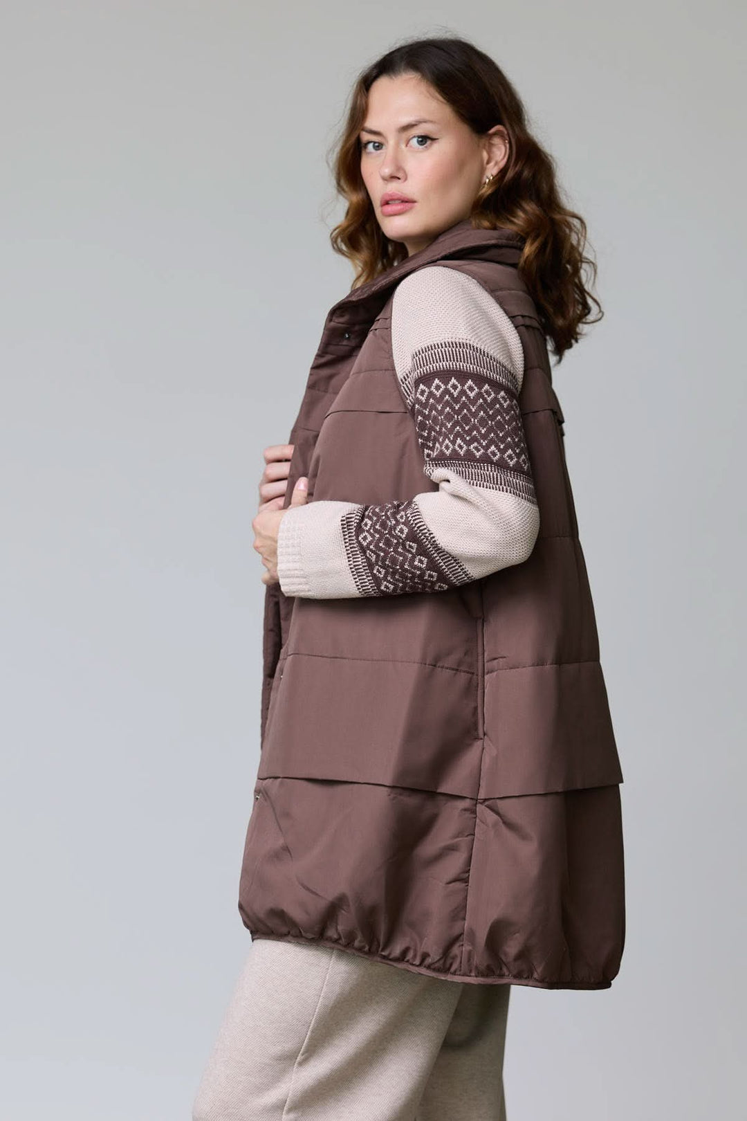 Veste sans manches matelassée brune portée de côté, design moderne et élégant, col montant et matelassage pour isolation. Description : Veste sans manches matelassée.