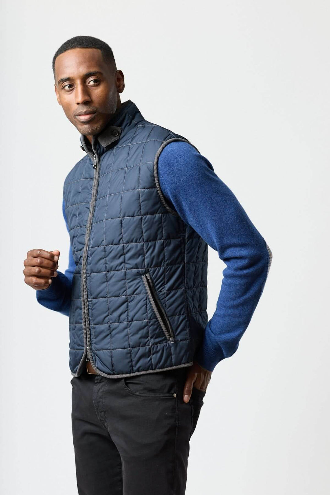 Homme portant une veste sans manches matelassée avec détails en velours côtelé, élégante et pratique, sur un chandail bleu.