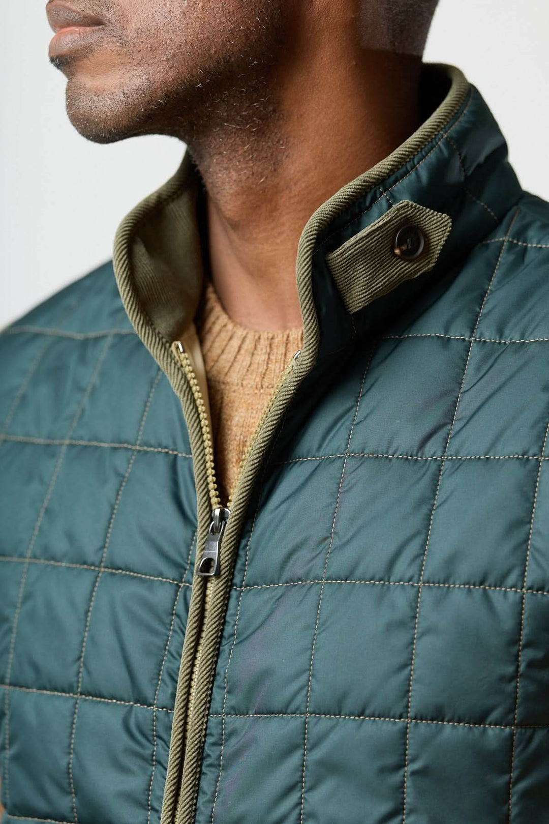 Homme portant une veste sans manches matelassée avec détails en velours côtelé, design élégant et fonctionnel en tissu résistant.