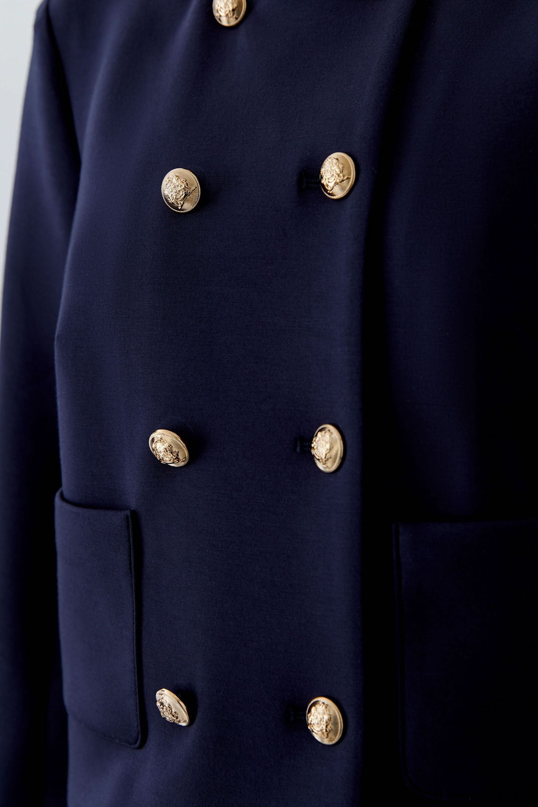 Veste structurée à boutons décoratifs en tissu bleu marine avec boutons métallisés dorés, style sophistiqué et chic.