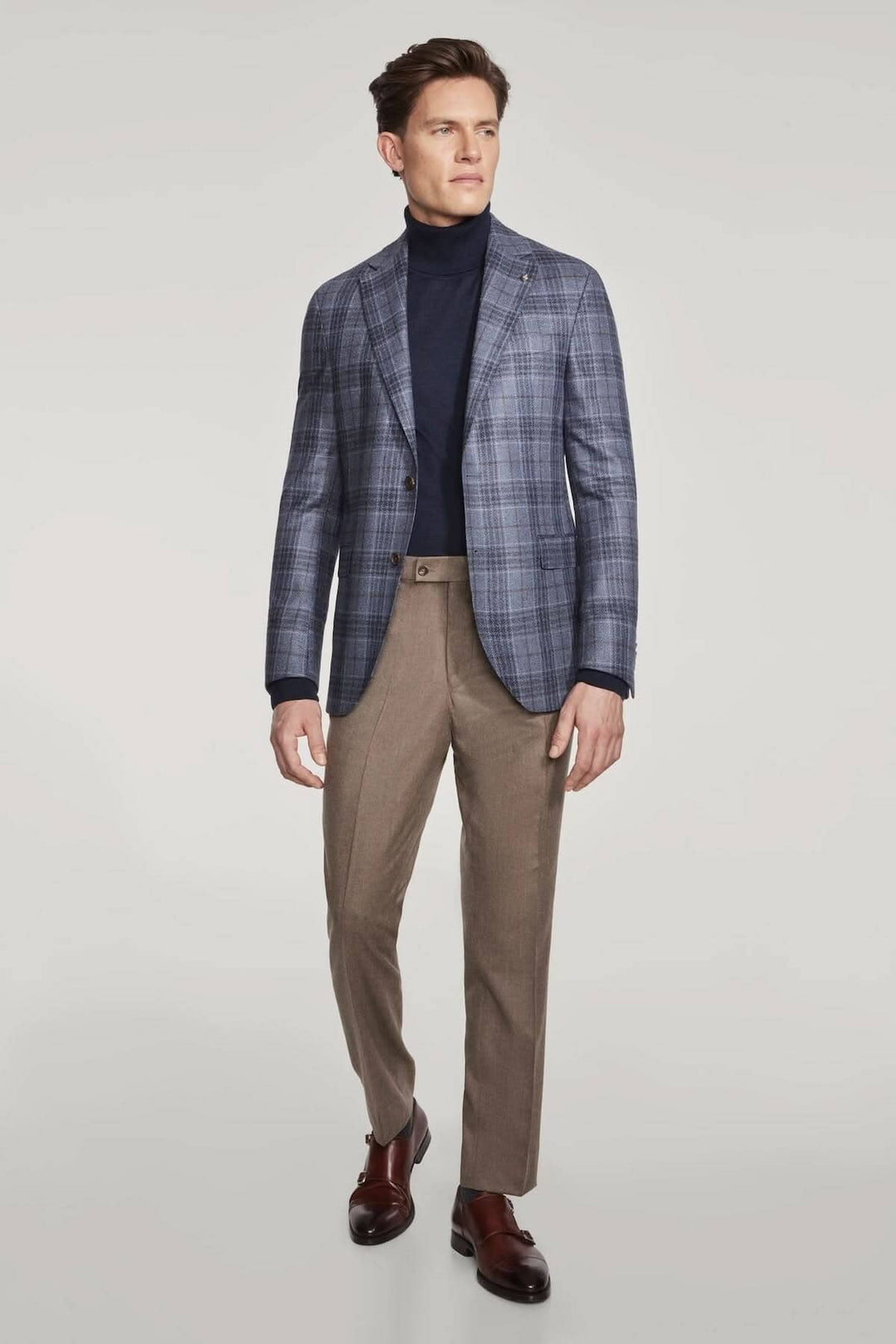 Veste à carreaux en laine et soie portée par un homme avec un pull bleu marine et un pantalon beige.
