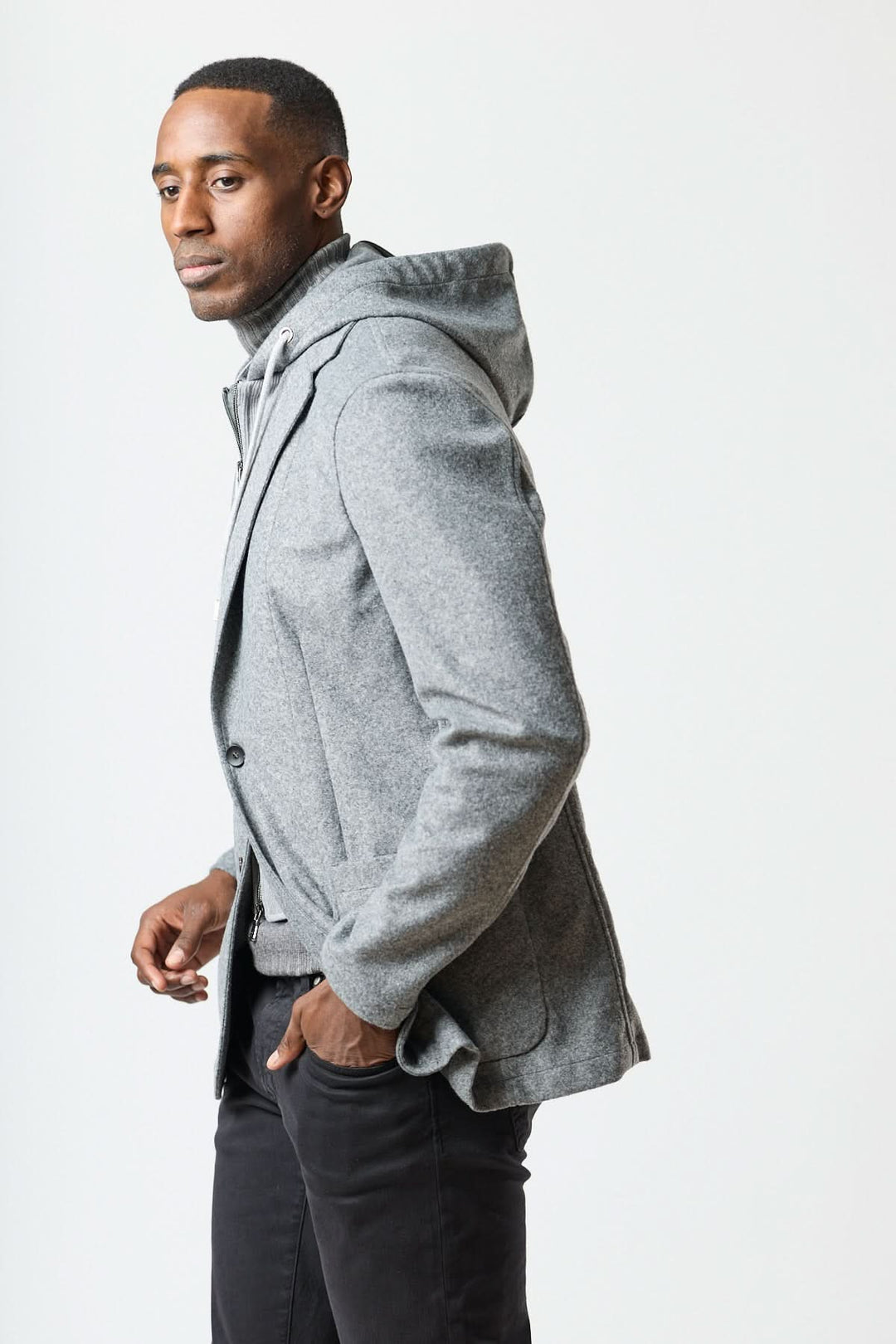 Homme portant un veston hybride à capuche en laine grise, combinant un blazer avec une capuche intégrée pour un style urbain chic.