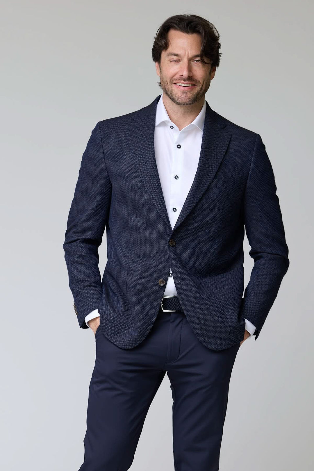 Homme portant un veston texturé à coupe moderne, bleu marine, avec chemise blanche et pantalon assorti, style élégant et contemporain.