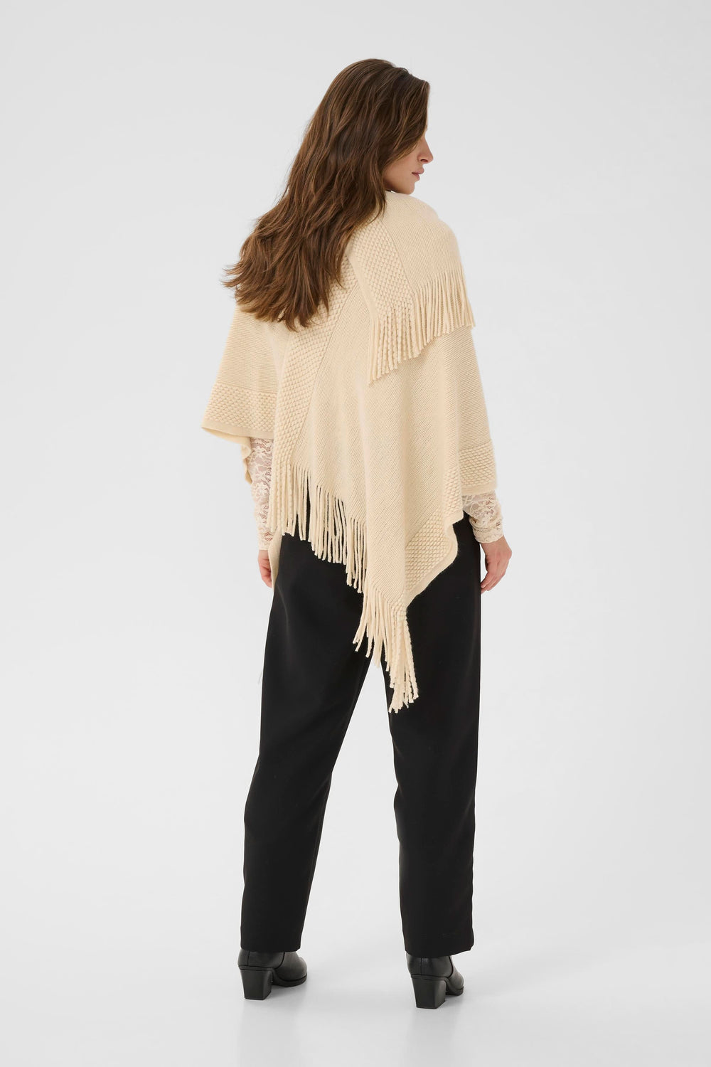 Femme portant une cape en tricot à franges beige, vue arrière, montrant sa texture douce et son style élégant avec un col drapé.