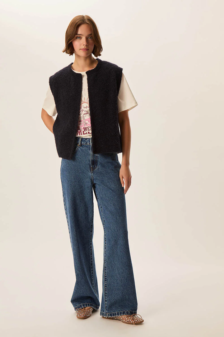 Femme portant la Veste Achille sans manches en laine bouclée, associée à un t-shirt imprimé et un jean décontracté.