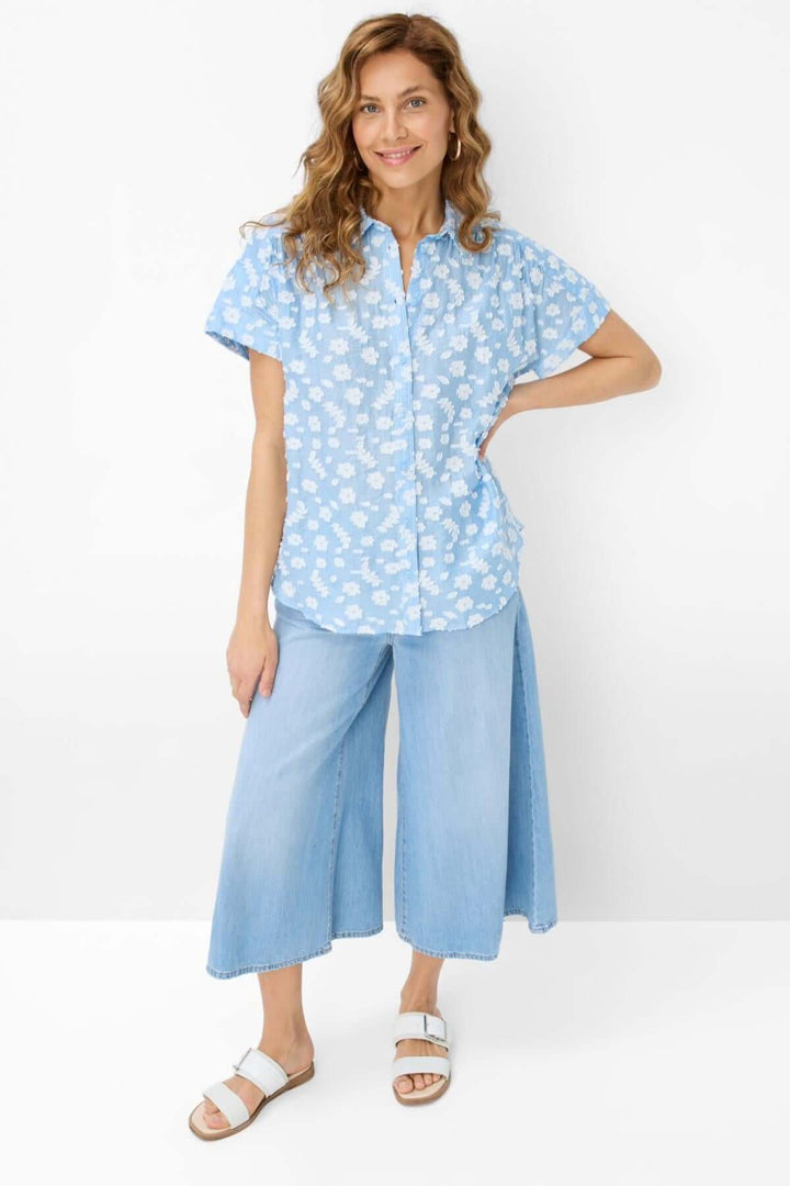 Blouse VIV broderie florale légère et élégante, portée avec un pantalon en denim, idéale pour l'été.