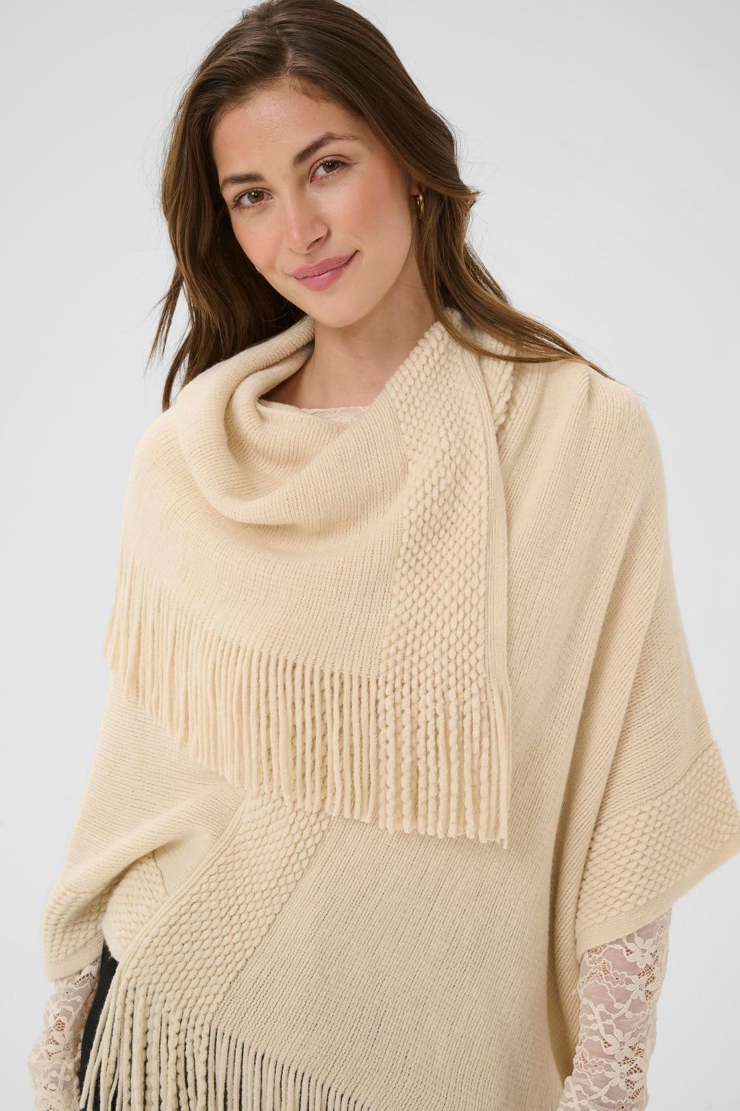Femme portant une cape en tricot à franges beige avec col drapé et texture douce, parfaite pour un style automnal élégant.