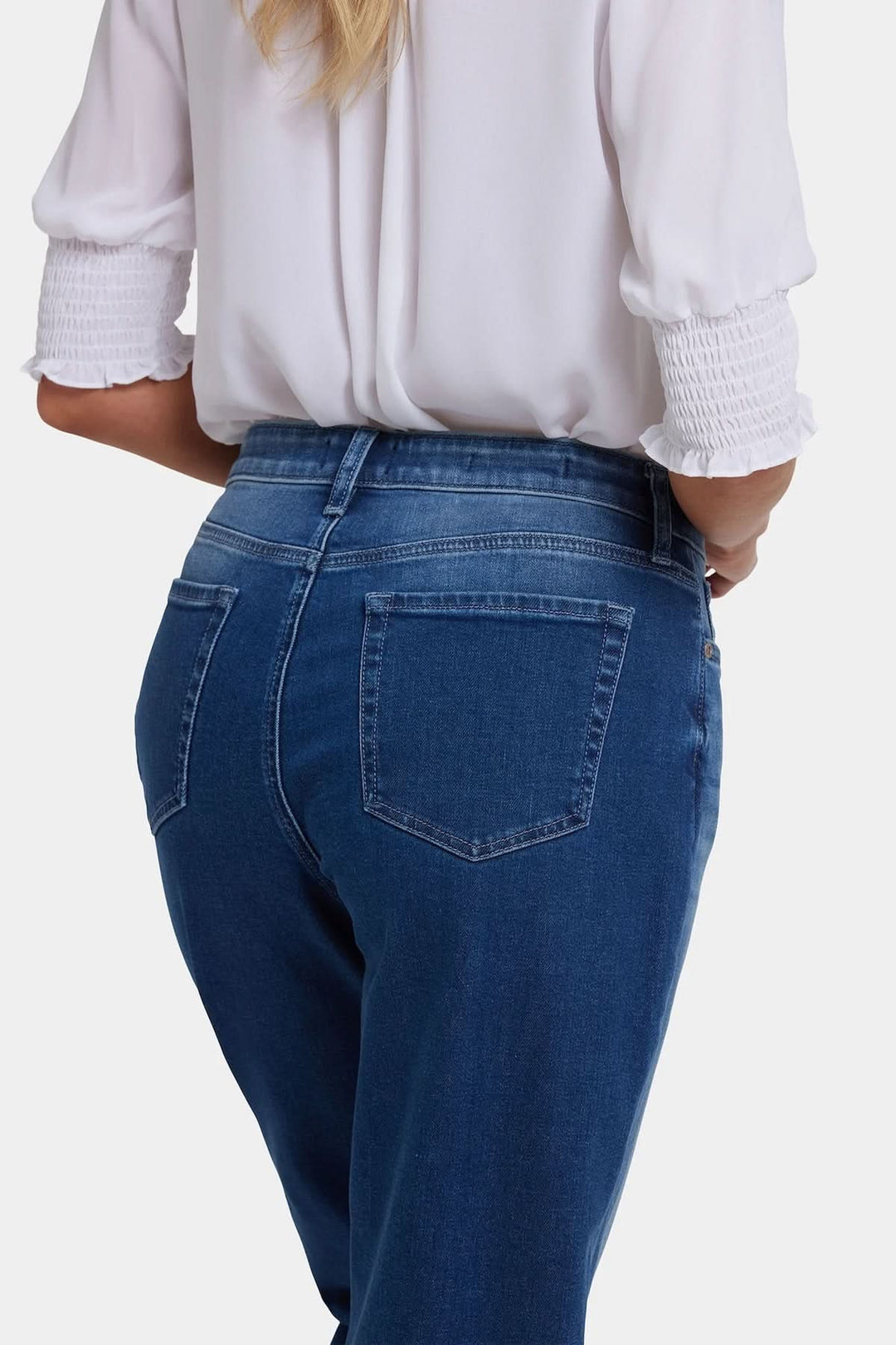 Jean boyfriend en bleu légèrement délavé avec coupe droite, taille classique, et passants de ceinture, porté avec une chemise blanche.