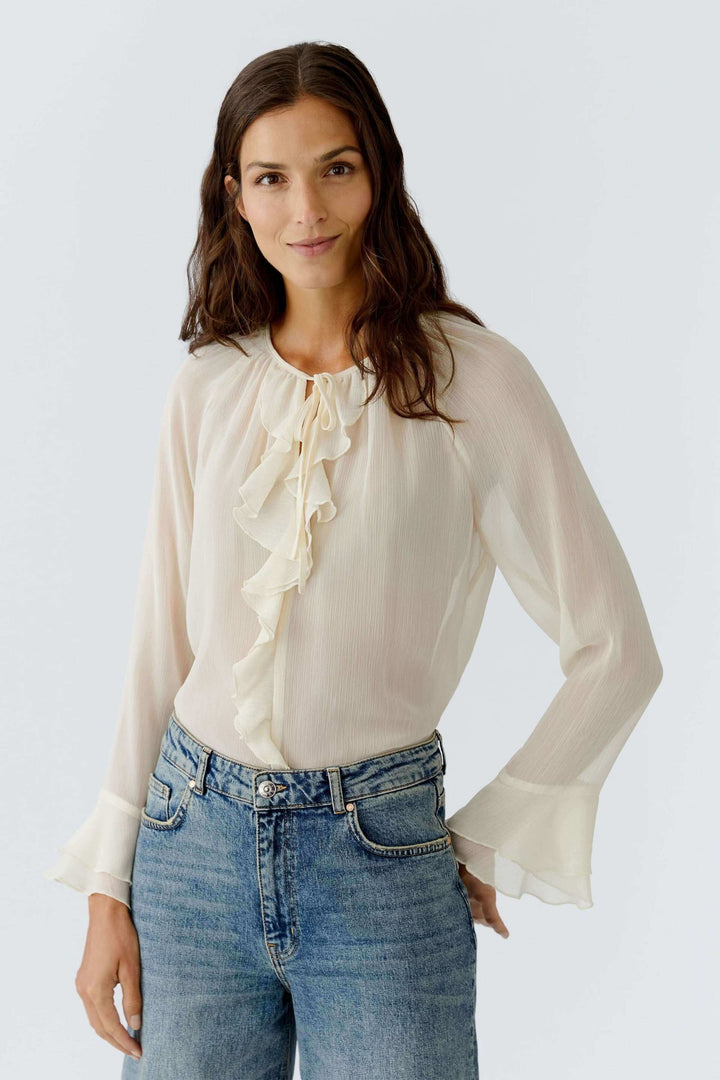 Blouse fluide à volants et lien au col, délicate et féminine, portée avec un jean pour un look chic et romantique.