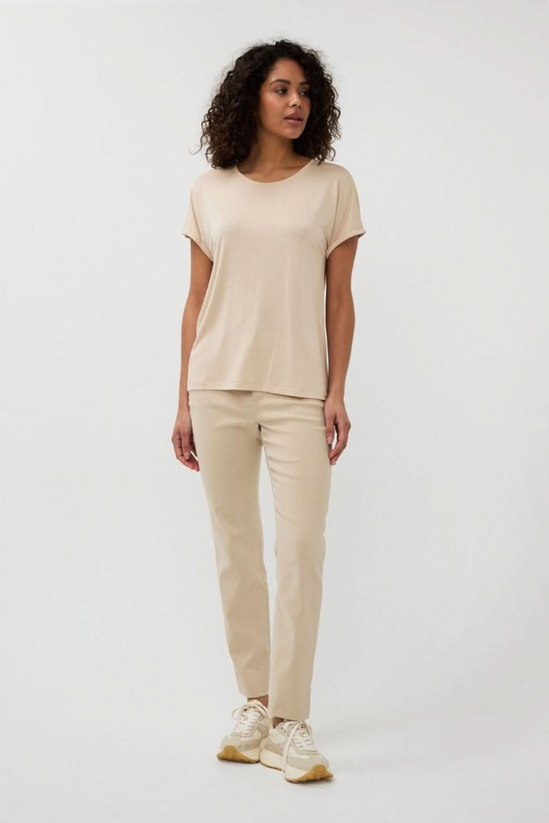 Femme portant un pantalon en jacquard texturé avec un haut beige et des sneakers, look chic-décontracté.