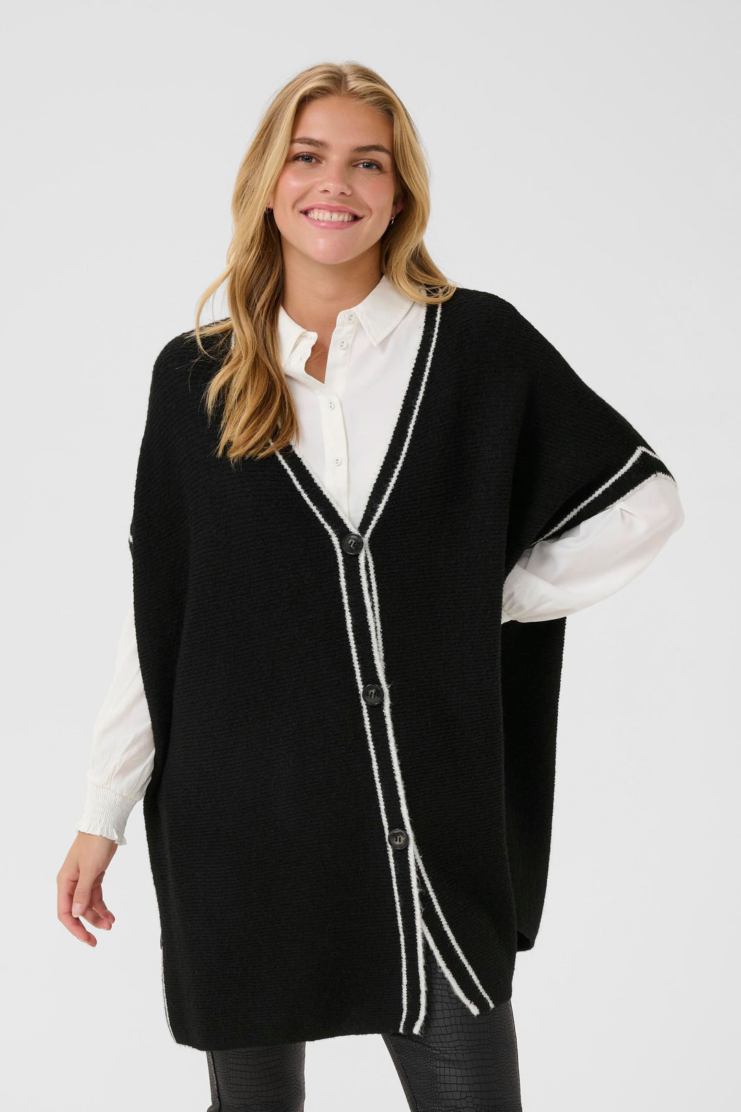 Cape Rams boutonnée en tricot à bord contrastant portée par une femme souriante, style chic et décontracté, encolure en V.