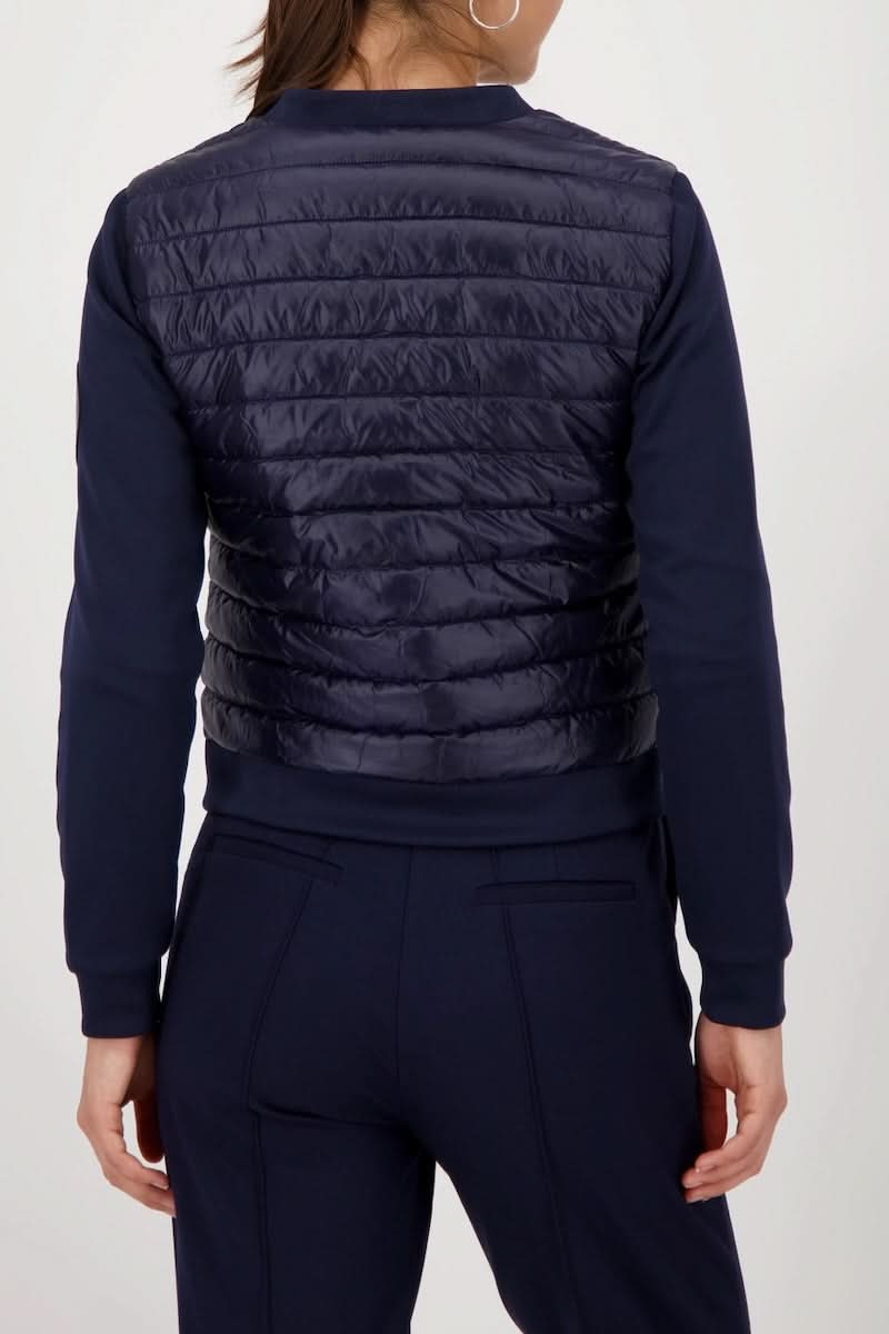 Femme portant une veste matelassée bimatière à fermeture éclair vue de dos, montrant le corps matelassé et les manches souples noires.
